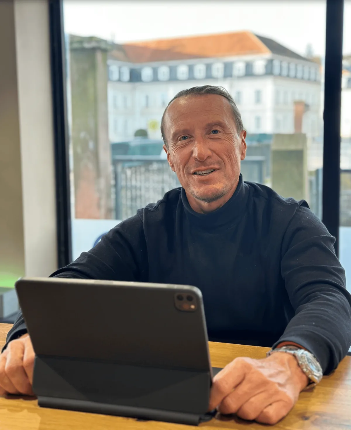 Lächelnder Mann im Rollkragenpullover am Tisch mit Tablet: Martin Tretter