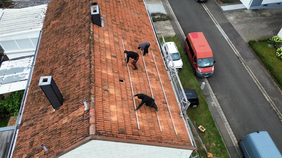 Drei Arbeiter installieren Solarmodule auf einem Ziegeldach